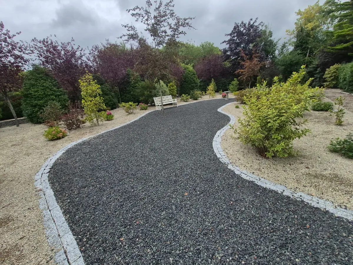 Curving dark gravel path edged with light granite setts through gravel beds planted with shrubs, a bench beyond