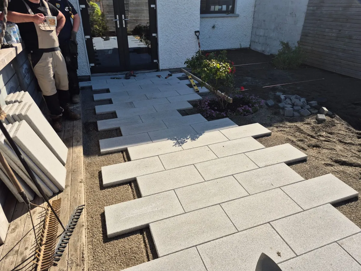 Pale grey porcelain planks laid in a stepped pattern leading from patio doors, with the bedding layer still visible at the edges