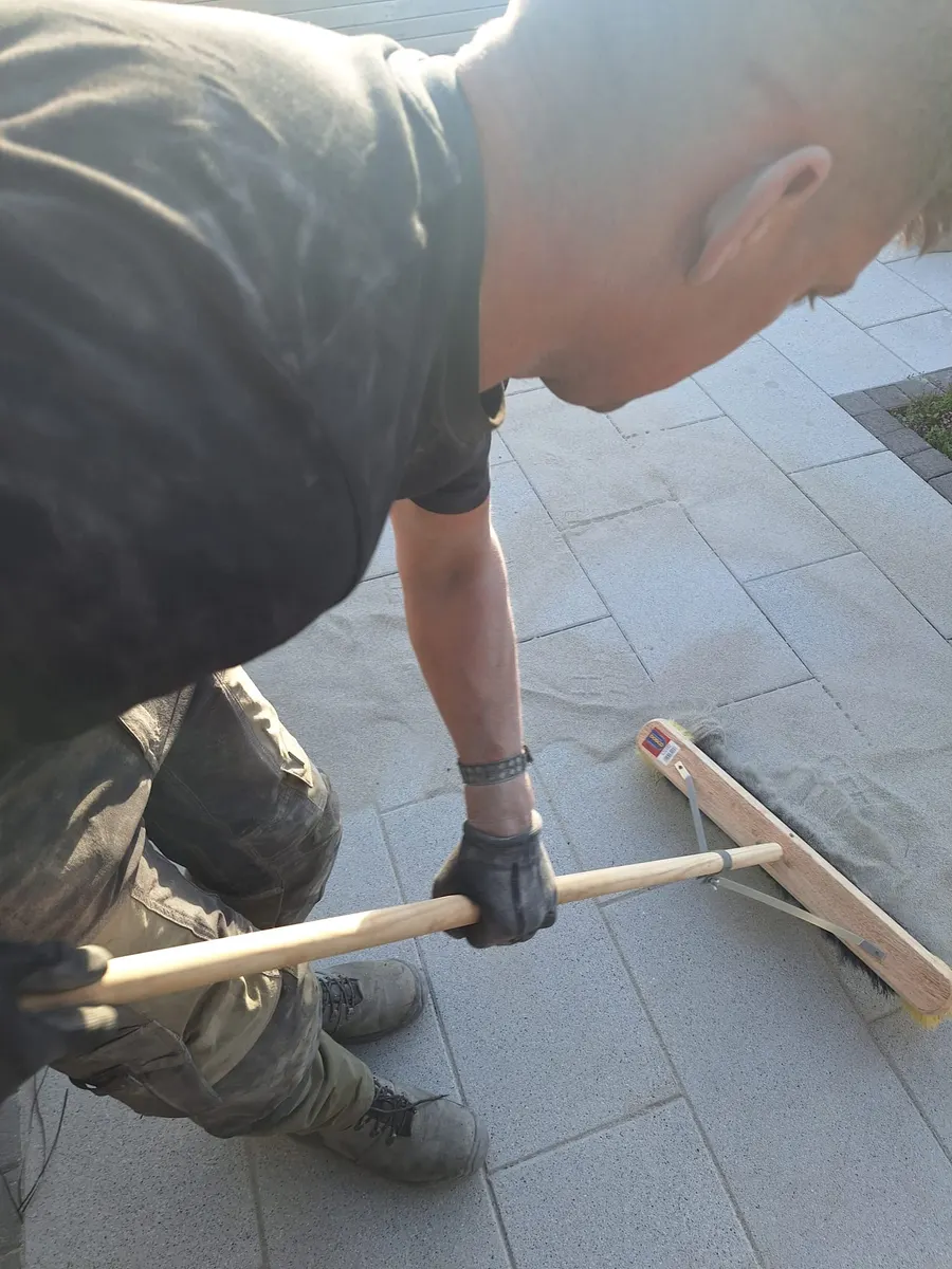 Landscaper brushing jointing sand across a newly laid pale grey patio