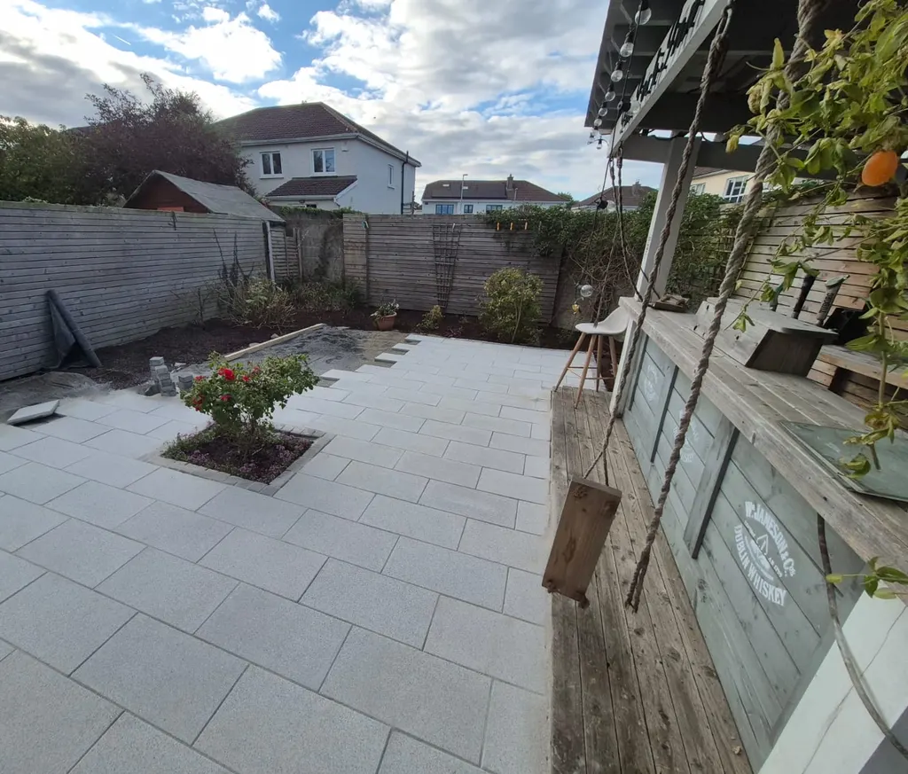 Wide view of a finished porcelain patio with a rose bed, timber bar and fenced garden