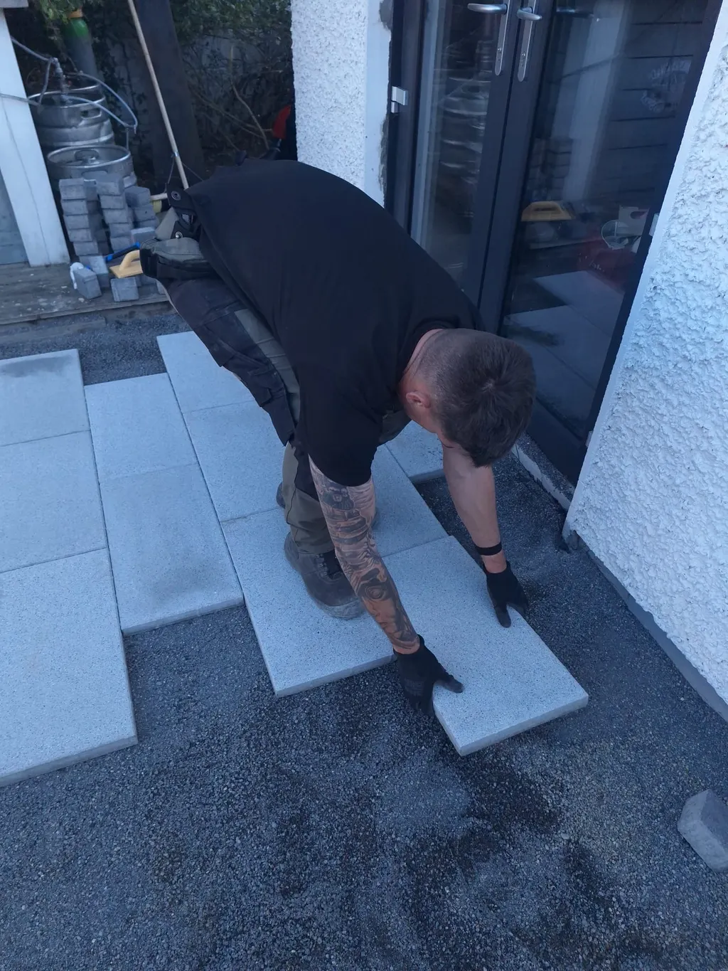 Landscaper lowering a porcelain slab into place on the bedding layer by patio doors