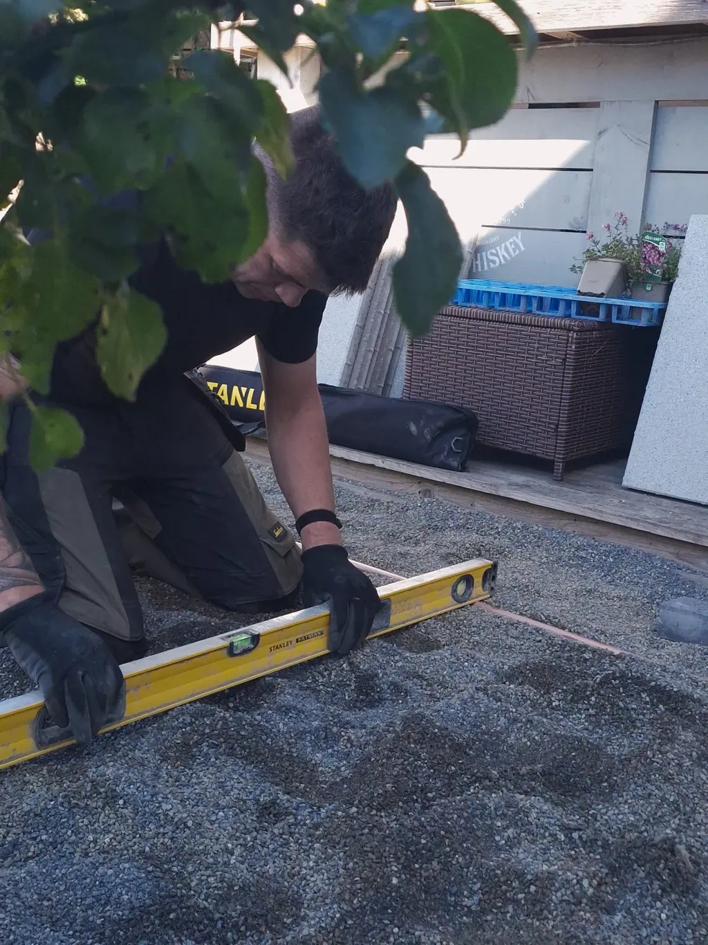 Landscaper kneeling with a spirit level on a screeded grit bed marked out with string lines