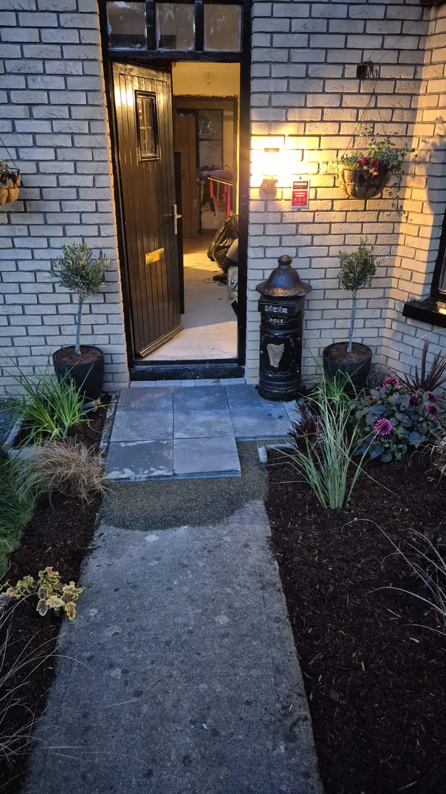 Front path at dusk to a lit black door, with new grasses in mulched beds